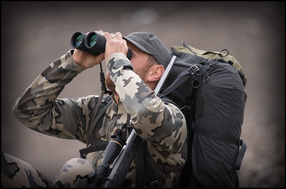 Man looking through binoculars in camo gear optics image
